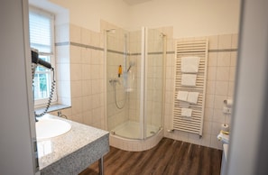 Un baño con ducha envuelta en vidrio, lavamanos con encimera de granito y toallero con varias toallas.