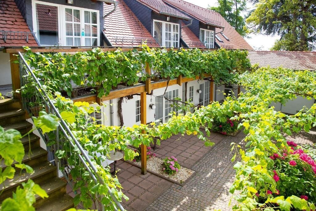Ein Wohngebäude mit überdachter Außenbereitschaft, einer Treppe und einem Garten mit verschiedenen Pflanzen.