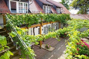 A residential building with a covered outdoor area featuring a staircase and a garden with various plants.