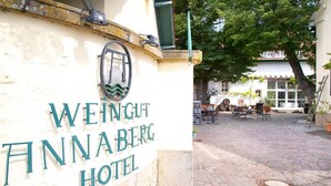 A sign for Weingut Annaberg Hotel with a stone wall and a paved courtyard.