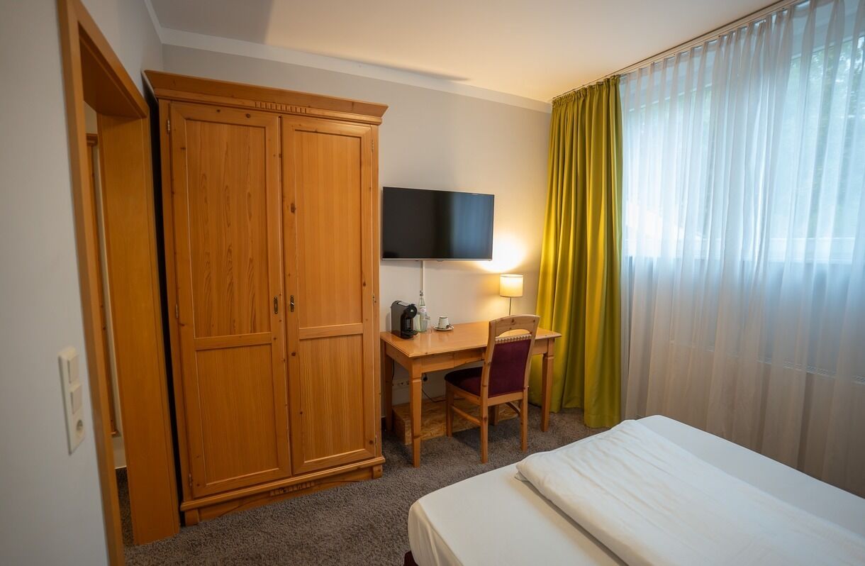 Une chambre d’hôtel comprenant un lit, un bureau avec une chaise, une télévision et une armoire.