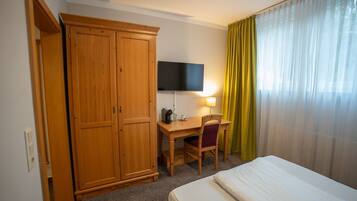 Ein Hotelzimmer mit einem Bett, einem Schreibtisch mit Stuhl, einem Fernseher und einem Kleiderschrank.