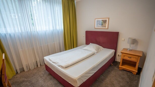A hotel room with a bed, a nightstand, a chair, and a window with curtains.