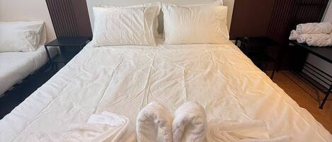 A neatly made bed with white linens and two towels folded on the bed.