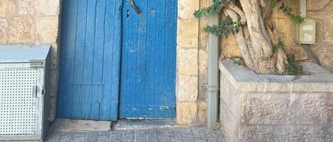 A blue door with a number plaque, a stone wall, and a tree with purple flowers.