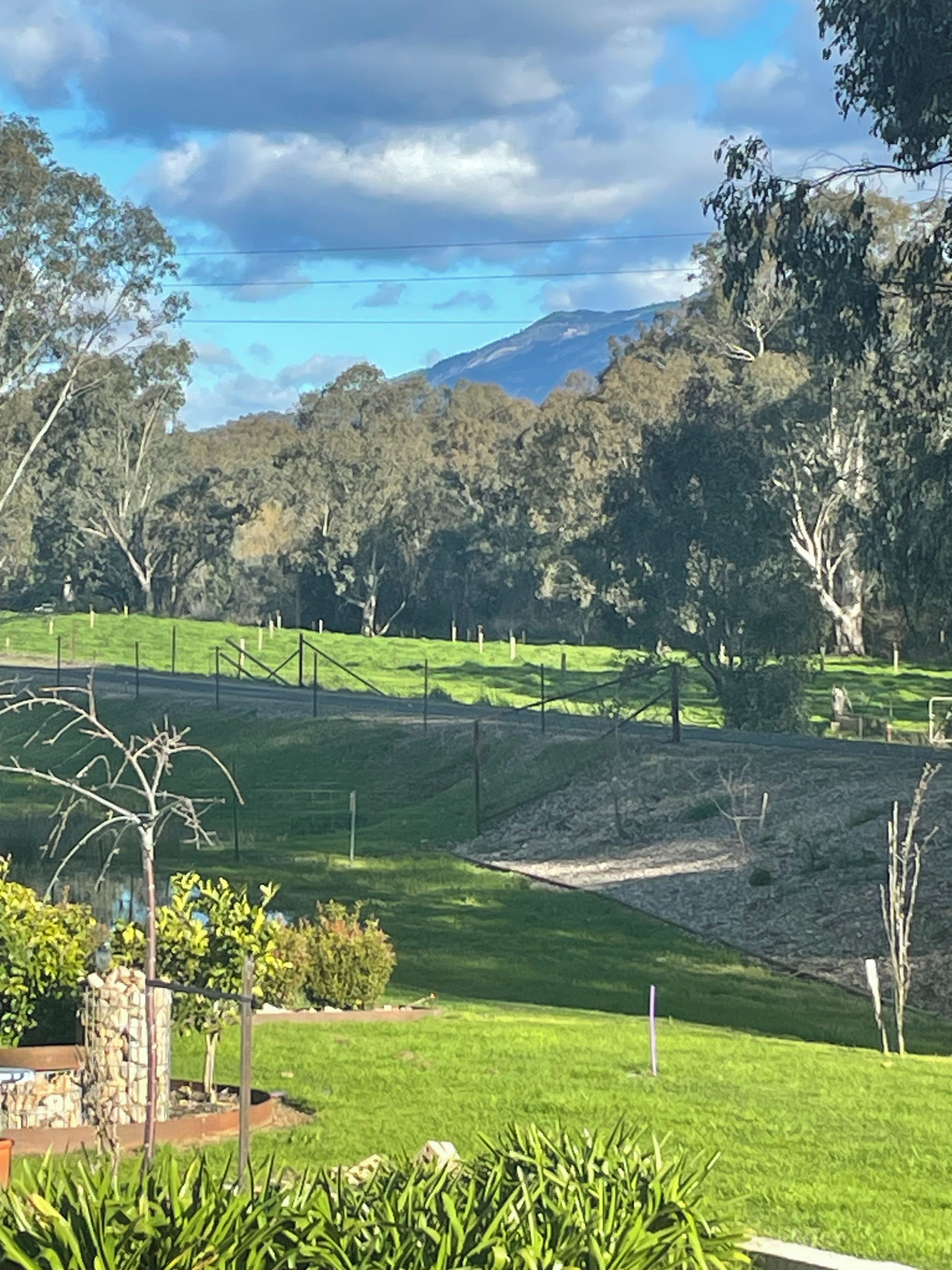 Un jardin aménagé avec une structure en pierre, un espace délimité par une clôture et une vue sur une chaîne de montagnes.