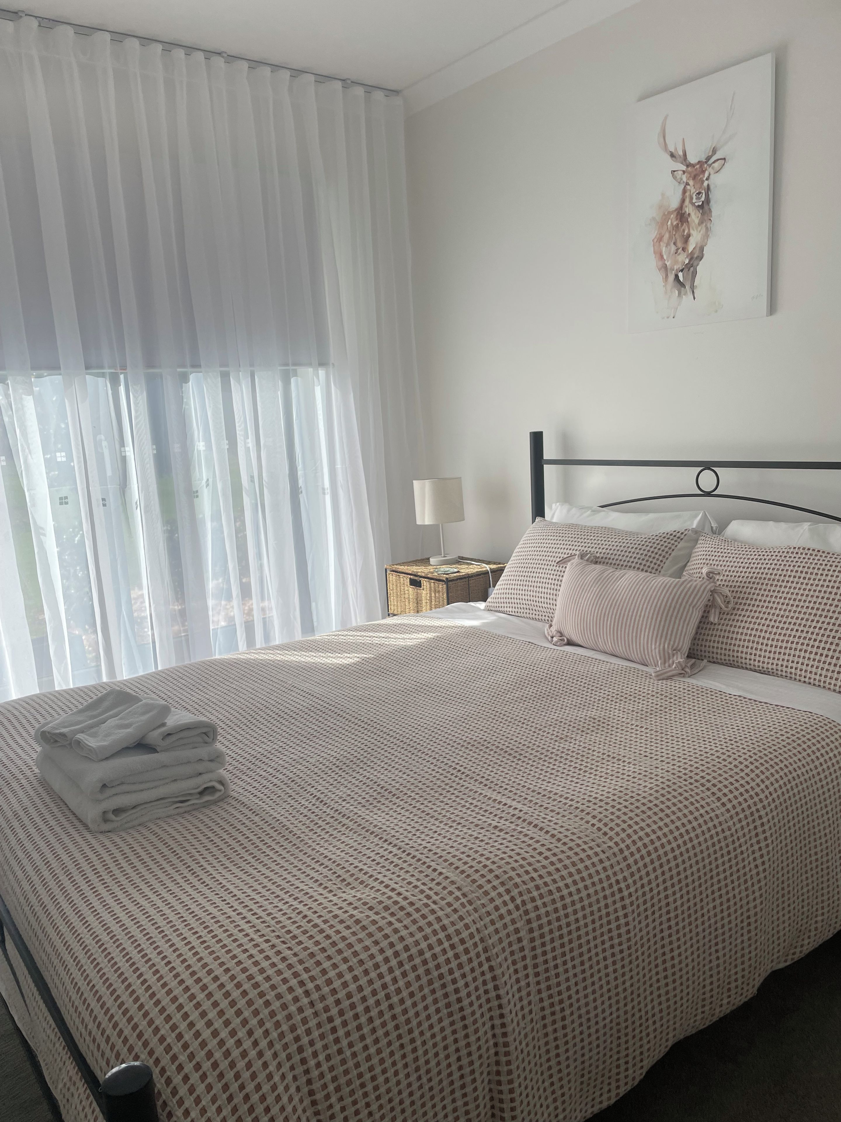 Un lit bien fait, recouvert d’une couvre-lit à motifs, une pile de serviettes pliées, une lampe de chevet et une œuvre d’art représentant un cerf, accrochée au mur.
