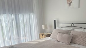 En pænt redt seng med et mønstret sengetæppe, en stak foldede håndklæder, en natlampe og et billede af et rådyr på væggen.
