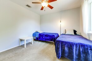 A bedroom with two beds, a ceiling fan, a bedside table, and a window with curtains. - Private Patio & Yard! Bastrop Retreat (Bastrop)
