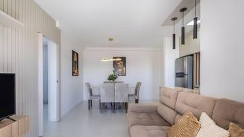 Una sala de estar moderna con un sofá color beige, un televisor de pantalla plana y una zona de comedor con mesa y sillas.