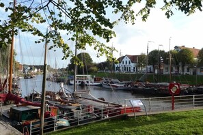 A marina with boats docked, a white building with a red roof, and a grassy area with a red sign. - Holiday apartment with 2 bedrooms (Wittmund)