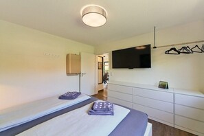 Una habitación de hotel con dos camas, un televisor montado en la pared, un perchero y un escritorio pequeño.