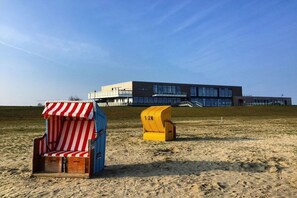 Une plage avec deux chaises de plage et un bâtiment moderne en arrière-plan.