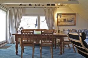 Un coin repas avec une table et des chaises en bois, une vue par la fenêtre et un tableau accroché au mur.