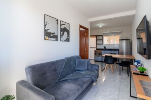 Ein modernes Wohnzimmer mit einem grauen Sofa, einem Holzesstisch und einer Küche im Hintergrund.
