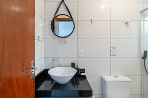Ein modernes Badezimmer mit einem weißen Waschbecken, einem runden Spiegel und einer Duschkabine aus Glas.