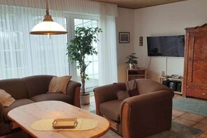 Ein Wohnzimmer mit einer Sofagarnitur, einem Holztisch, einer Topfpflanze, einem Fernseher und einem Schrank.