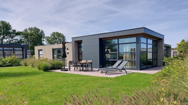 Ein modernes Haus mit Terrasse, Gartenmöbeln und Rasen.
