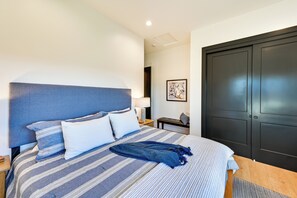 A neatly made bed with striped bedding and a blue headboard, a bedside table with a lamp, and a dark door. - Golf Views, Resort Pool Access! Brasada Ranch Home (Powell Butte)