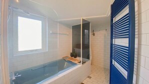 Une salle de bain avec une baignoire, une fenêtre et un espace douche.