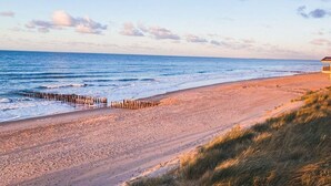Une plage avec une jetée en bois, un rivage sablonneux et un bâtiment en arrière-plan.