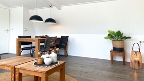Un coin repas avec une table et des chaises en bois, des lampes suspendues, une plante en pot et un petit tabouret.