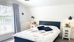 Une chambre à coucher avec un lit, des lampes de chevet, une fenêtre avec des rideaux et un radiateur.