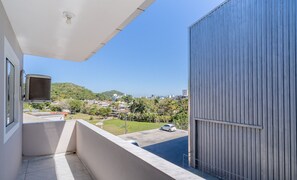 A balcony with a view of a residential area, a parked car, and a building with a corrugated metal exterior. - Charming Apartment in Jurere Jma011 (Florianópolis)