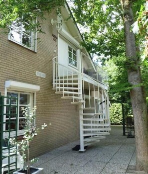 Ein zweistöckiges Gebäude mit weißer Fassade, einem Balkon und einem kleinen Garten.