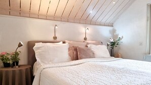 Quarto com cama, mesas de cabeceira e luminárias fixadas na parede.