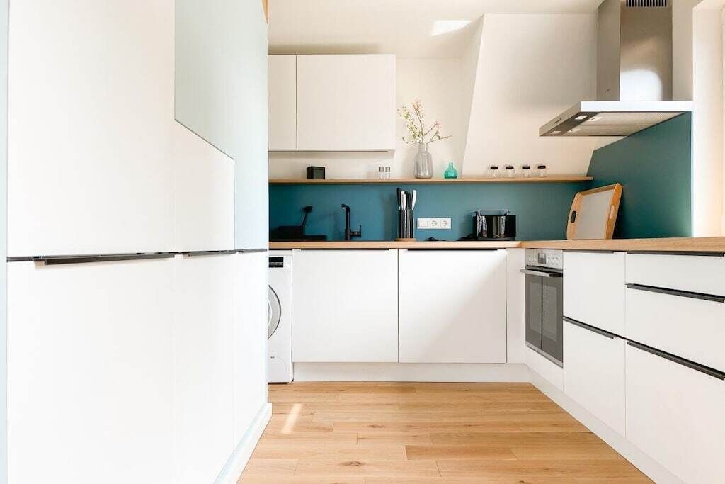 Une cuisine moderne avec des armoires blanches, un plan de travail en bois et un four encastré.