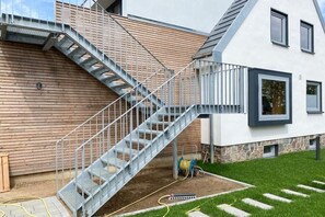Una casa moderna con una escalera de metal que conduce a una terraza de madera.