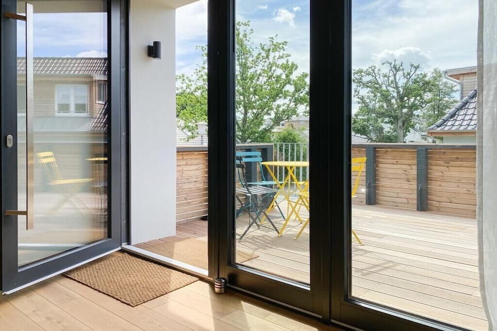 A room with a sliding glass door leading to an outdoor deck with a wooden floor and a yellow table and chairs.
