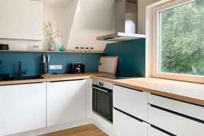 A modern kitchen with white cabinets, a black oven, and a window with a view of greenery. - Holiday apartment with 3 bedrooms (Scharbeutz)