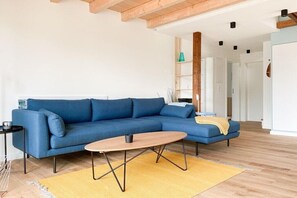 Una sala moderna con un sofá seccional azul, una mesa de centro de madera y una alfombra amarilla.