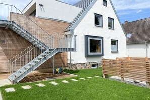 Una casa moderna con una escalera que conduce a una terraza de madera, un banco y un césped cuidado.