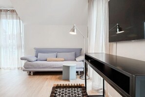 A modern living room with a sofa, a small side table, a black entertainment unit, and two floor lamps. - Four Seasons||Timmendorfer Strand (Timmendorfer Strand\/Niendorf)