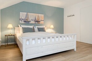 A bedroom with a white bed, two bedside tables with lamps, a wall-mounted painting, and a white door. - Four Seasons||Timmendorfer Strand (Timmendorfer Strand\/Niendorf)