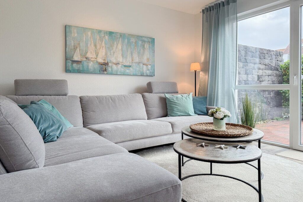 A living room with a grey sofa, a round coffee table with a vase, and a painting of sailboats on the wall.