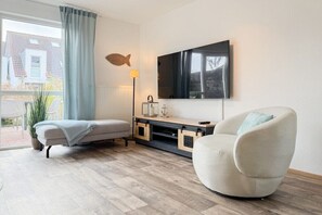 A modern living room with a sofa, a chair, a flat-screen TV, a lamp, and a fish decoration on the wall. - Four Seasons||Timmendorfer Strand (Timmendorfer Strand\/Niendorf)