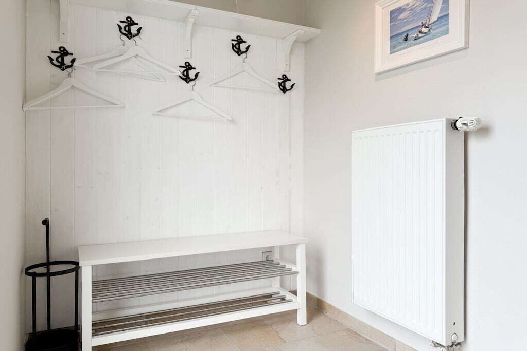 Un banc en bois peint en blanc, doté d’étagères en métal, d’un radiateur et de crochets muraux en forme d’ancre, également peints en noir.