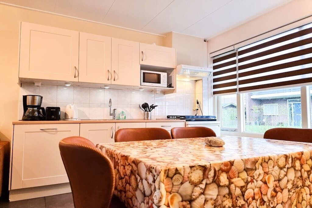 Cozinha moderna com armários brancos, micro-ondas e área de refeições com mesa coberta por toalha estampada com conchas.