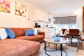 Een moderne woonkamer met een bruine bank, een salontafel en een eethoek met stoelen.