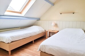 Een slaapkamer met twee bedden, een dakraam, een nachtkastje met een lamp en een houten vloer.