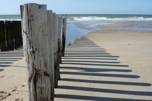 Een strand met houten palen en een zandpad dat naar het water leidt.
