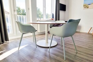Une pièce avec une table ronde, deux chaises, un téléviseur fixé au mur et une fenêtre avec des rideaux.