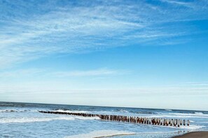 Ein Strand mit einem hölzernen Wellenbrecher, der ins Meer hineinreicht.