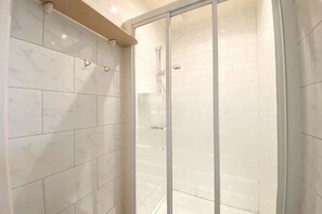 Ein Badezimmer mit weißen Marmorfliesen, einer Duschkabine aus Glas und einem beige gefärbten Handtuchhalter.