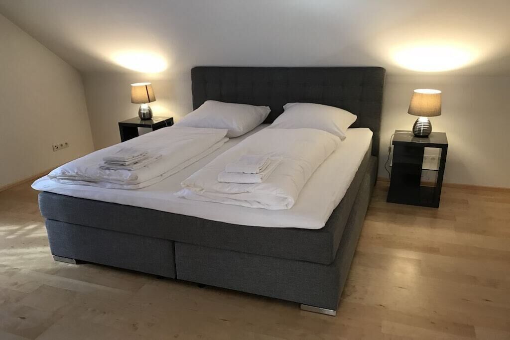 A neatly made double bed with white linens, two bedside tables with lamps, and a dark headboard.