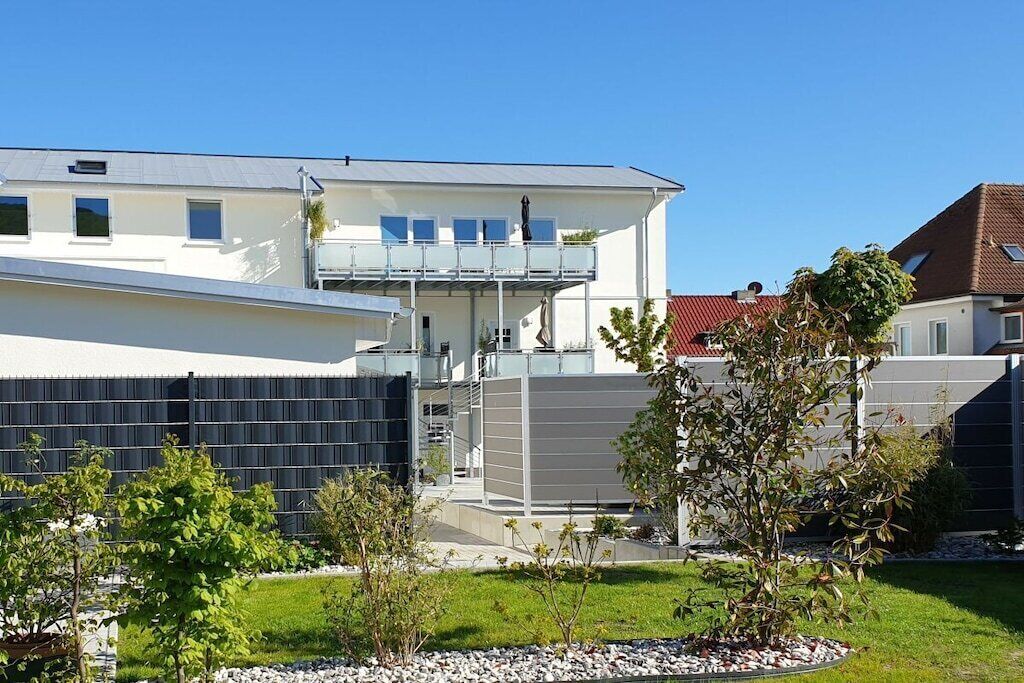 A modern two-story house with a balcony, a flat roof, and a well-maintained garden.